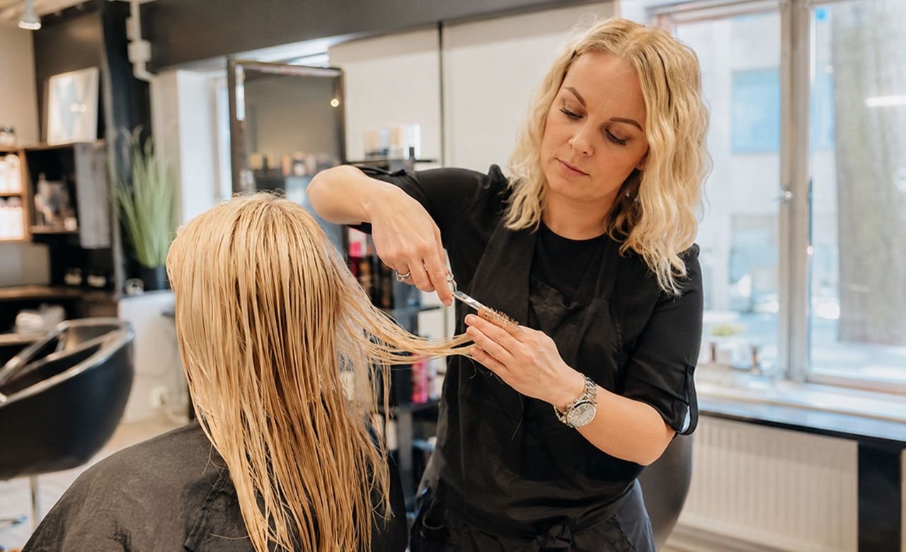kuva suomalaisesta kampaajasta leikkaamassa asiakkaan hiuksia modernissa kampaamossa.