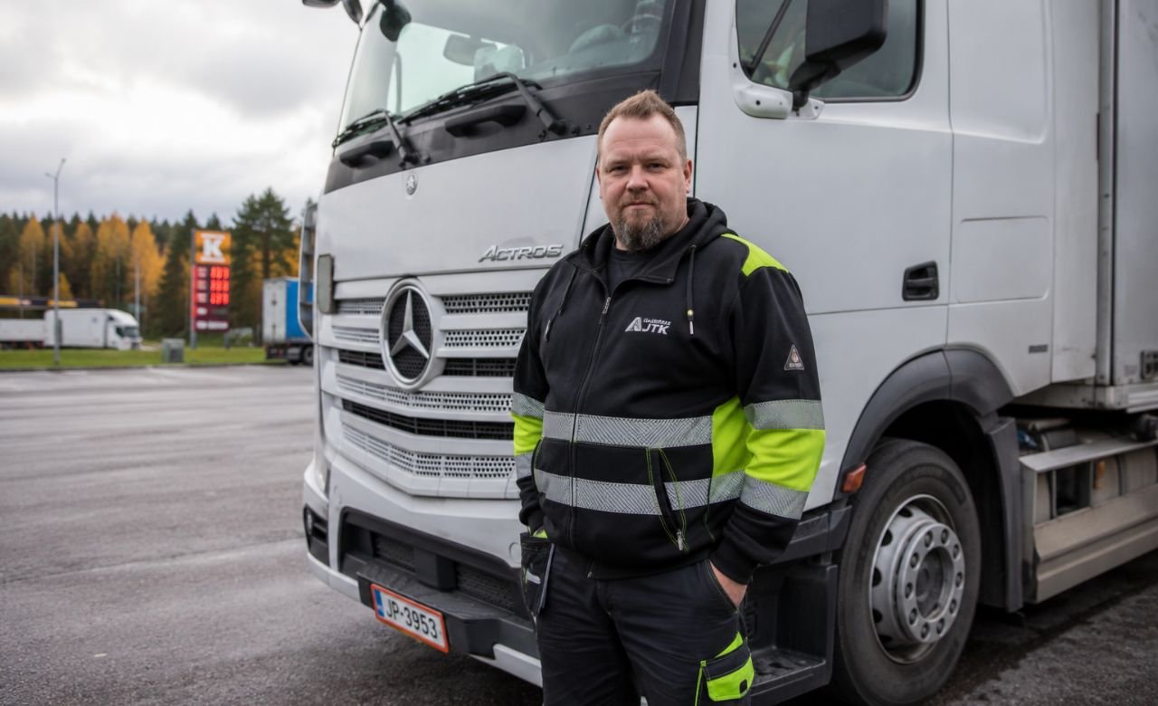 kuva suomalaisesta rekka-autonkuljettajasta seisomassa rekka-auton vieressä suomalaisella tienvarressa.