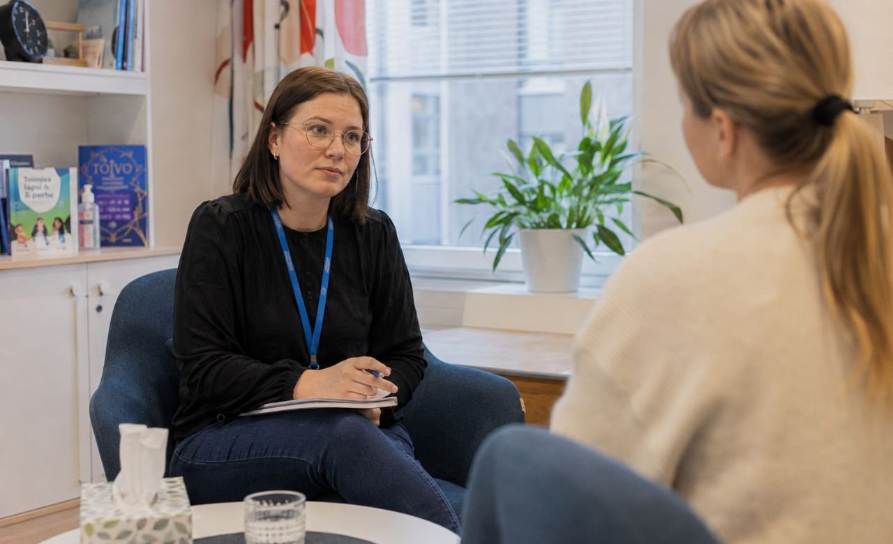 kuva suomalaisesta sosionomista asiakastapaamisessa modernissa sosiaalipalvelutoimistossa.