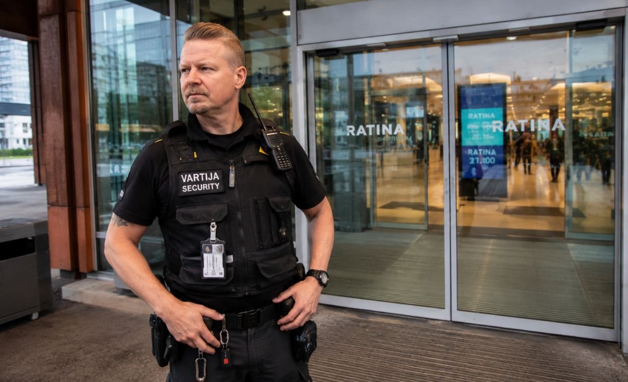 kuva suomalaisesta vartijasta seisomassa kauppakeskuksen tai toimistorakennuksen sisäänkäynnillä.