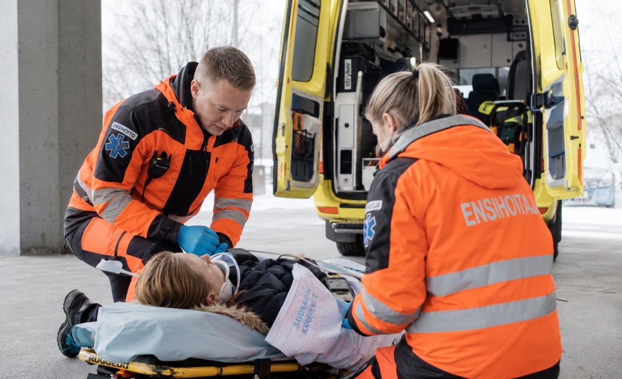 kuva suomalaisista ensihoitajista hoitamassa potilasta ambulanssin vieressä.